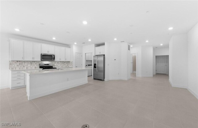 kitchen with tasteful backsplash, light tile patterned floors, stainless steel appliances, a center island with sink, and white cabinets