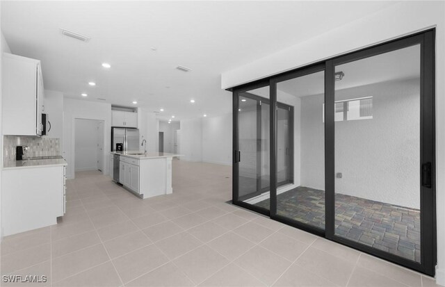 kitchen with light tile patterned floors, appliances with stainless steel finishes, tasteful backsplash, an island with sink, and white cabinetry