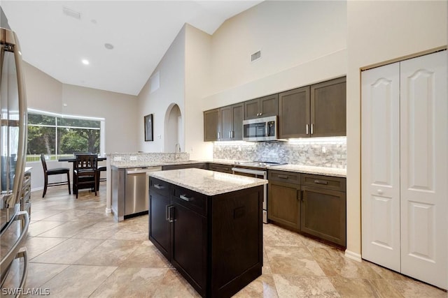 kitchen with appliances with stainless steel finishes, a kitchen island, kitchen peninsula, high vaulted ceiling, and dark brown cabinets