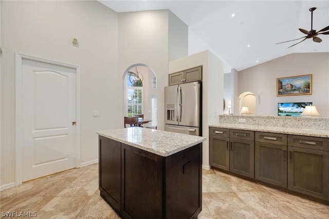 kitchen with a center island, dark brown cabinetry, ceiling fan, light stone counters, and stainless steel fridge