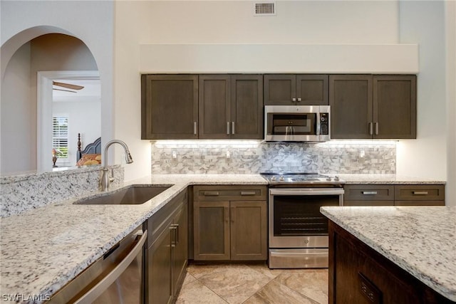 kitchen featuring light stone countertops, appliances with stainless steel finishes, tasteful backsplash, sink, and dark brown cabinets