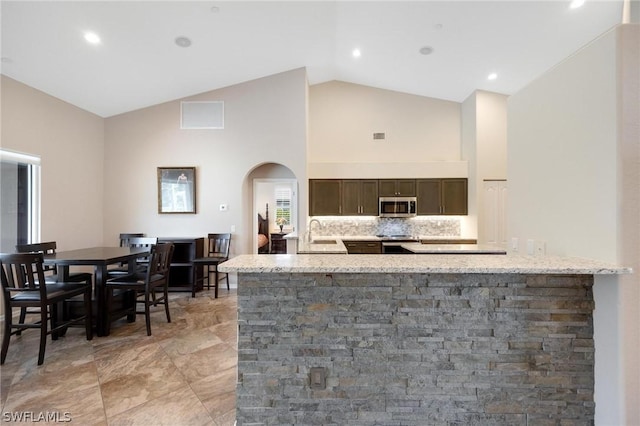 kitchen with high vaulted ceiling, light stone counters, appliances with stainless steel finishes, and tasteful backsplash