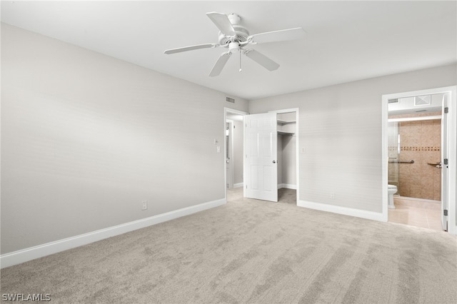 unfurnished bedroom featuring ceiling fan, a spacious closet, ensuite bathroom, carpet floors, and a closet