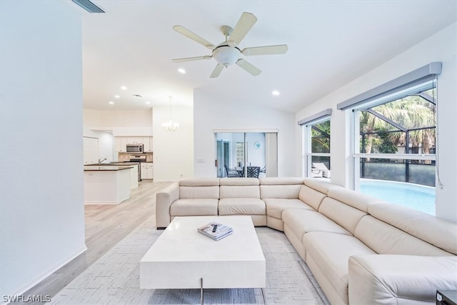 living room with sink, lofted ceiling, light hardwood / wood-style flooring, and ceiling fan with notable chandelier