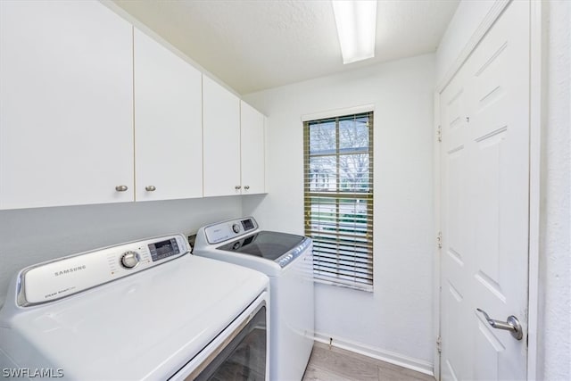 clothes washing area with cabinets, light hardwood / wood-style flooring, and washing machine and clothes dryer