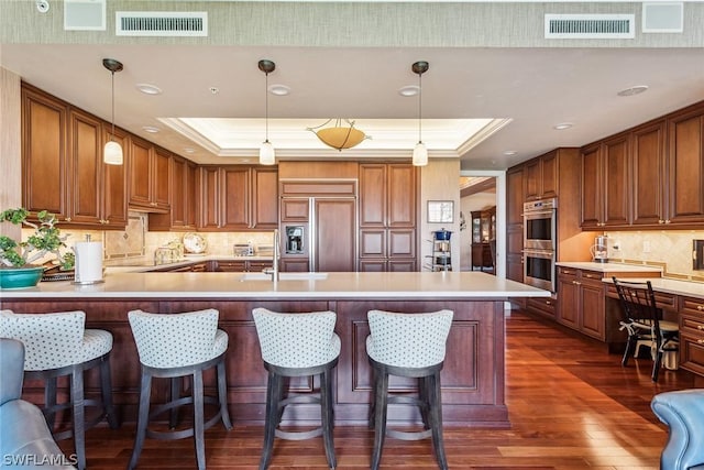 kitchen featuring paneled built in fridge, stainless steel double oven, hanging light fixtures, and a tray ceiling