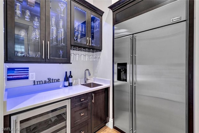 bar with built in fridge, beverage cooler, a sink, light wood-type flooring, and indoor wet bar