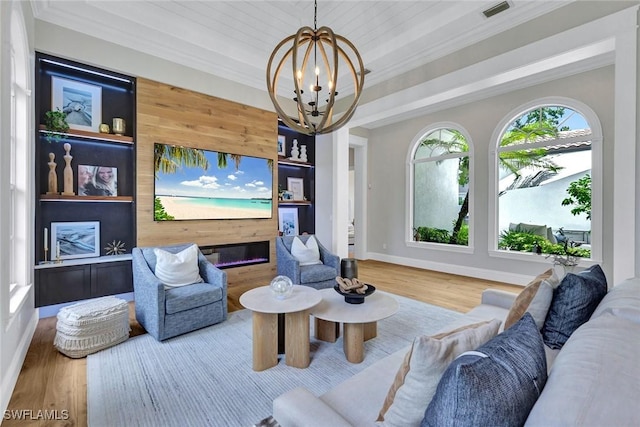 living area featuring wood finished floors, visible vents, an inviting chandelier, a glass covered fireplace, and crown molding