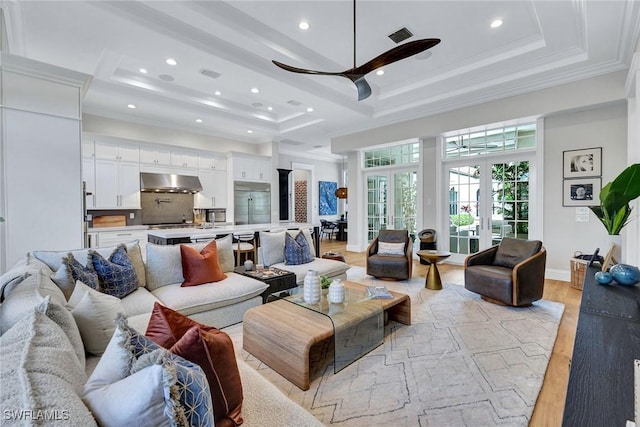 living area with a tray ceiling, french doors, crown molding, and light wood-style flooring