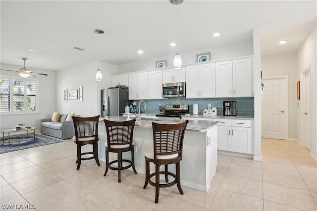 kitchen with appliances with stainless steel finishes, a kitchen breakfast bar, light stone counters, pendant lighting, and an island with sink