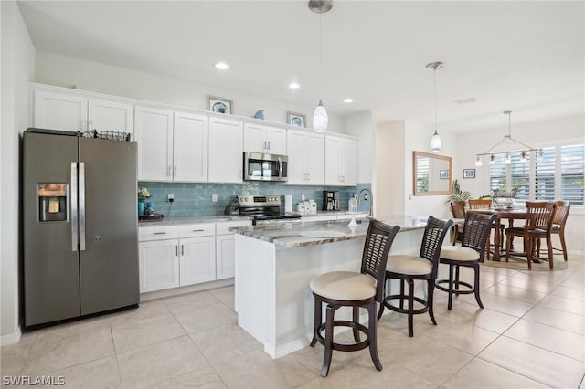 kitchen featuring pendant lighting, a center island with sink, light stone counters, white cabinetry, and stainless steel appliances