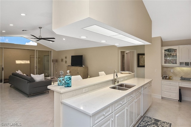 kitchen with vaulted ceiling with skylight, ceiling fan, white cabinetry, and sink