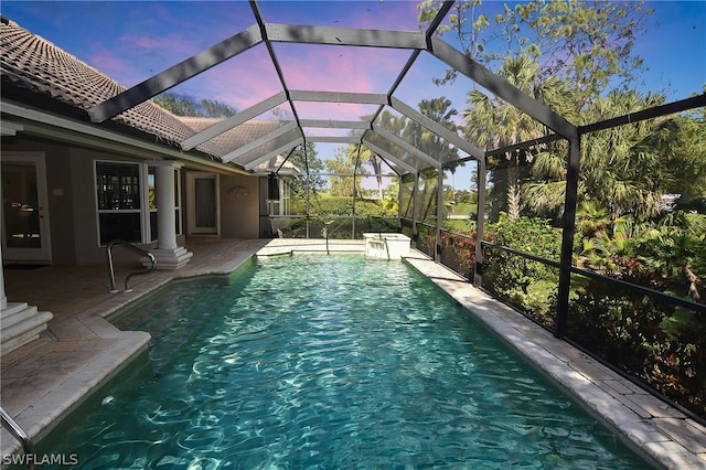 pool at dusk with glass enclosure and a patio area