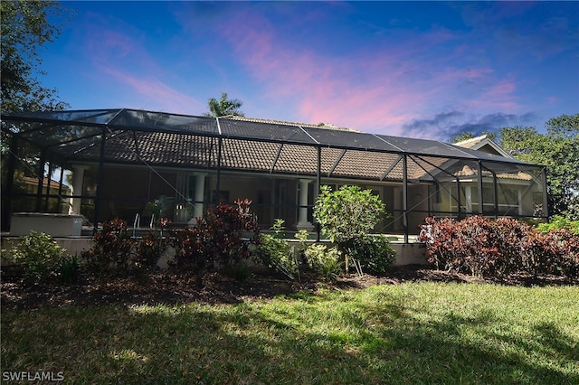 back house at dusk featuring glass enclosure and a yard