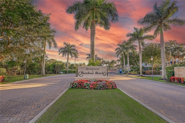 community sign featuring decorative driveway and a yard