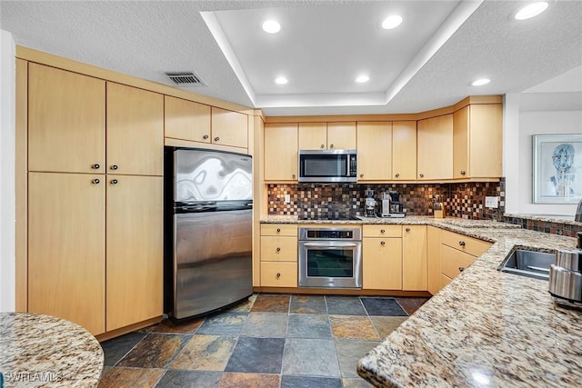 kitchen with backsplash, appliances with stainless steel finishes, light stone counters, and light brown cabinetry
