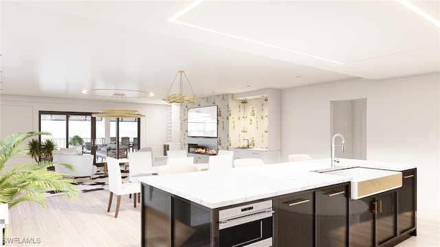 kitchen with sink, a kitchen island with sink, pendant lighting, oven, and light hardwood / wood-style floors