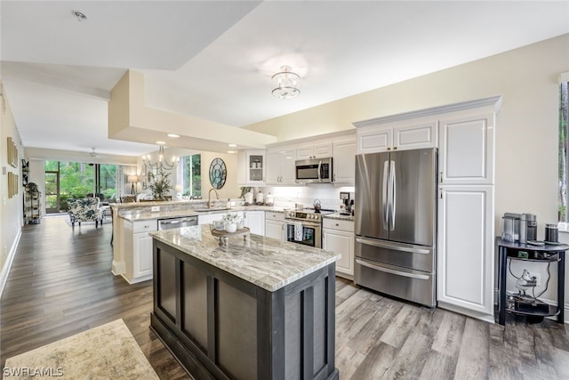 kitchen featuring a notable chandelier, a peninsula, white cabinets, appliances with stainless steel finishes, and glass insert cabinets