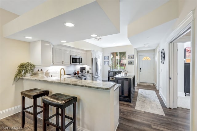 kitchen featuring light stone counters, decorative backsplash, appliances with stainless steel finishes, white cabinetry, and a peninsula