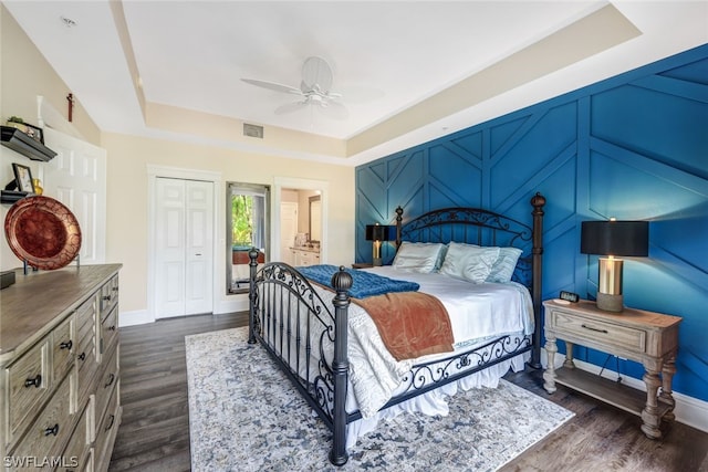 bedroom featuring a ceiling fan, visible vents, baseboards, a tray ceiling, and dark wood finished floors