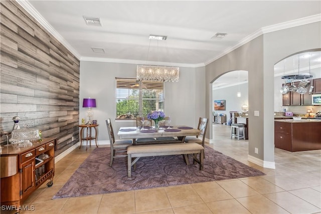 dining space with ornamental molding, wood walls, a notable chandelier, and light tile patterned floors