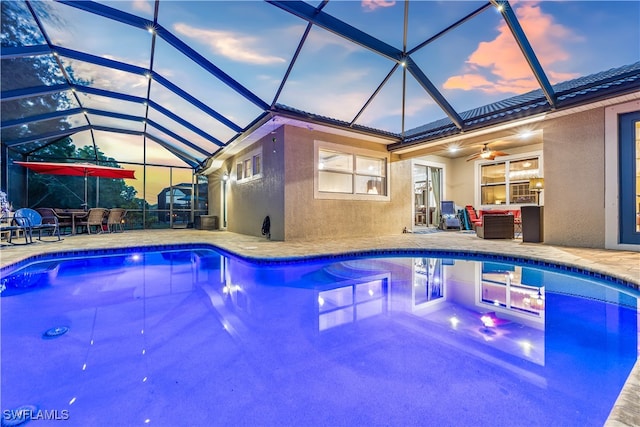 pool at dusk with ceiling fan, a lanai, and a patio