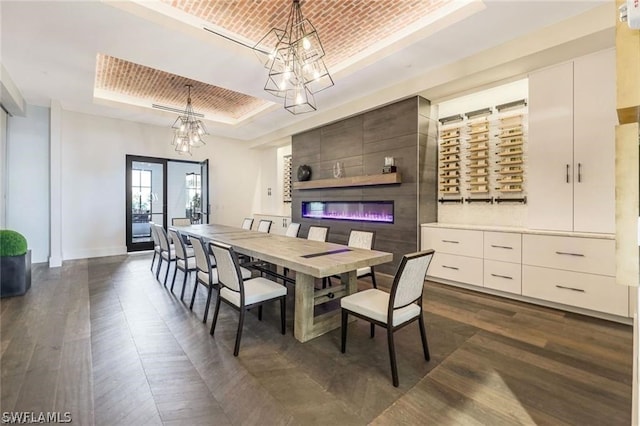 dining room featuring dark hardwood / wood-style flooring, a notable chandelier, a tile fireplace, and a raised ceiling