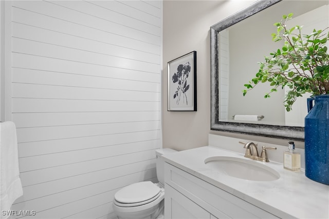 bathroom featuring vanity, toilet, and wood walls