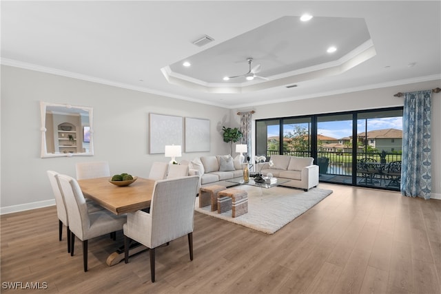 dining space featuring light hardwood / wood-style floors, a raised ceiling, ornamental molding, and ceiling fan