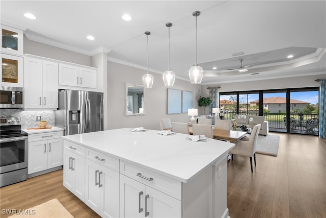 kitchen with hanging light fixtures, a center island, white cabinets, appliances with stainless steel finishes, and light hardwood / wood-style floors