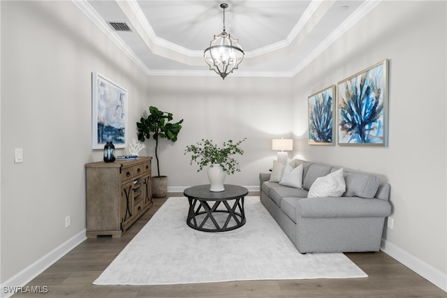 living room featuring hardwood / wood-style flooring, ornamental molding, a tray ceiling, and a chandelier