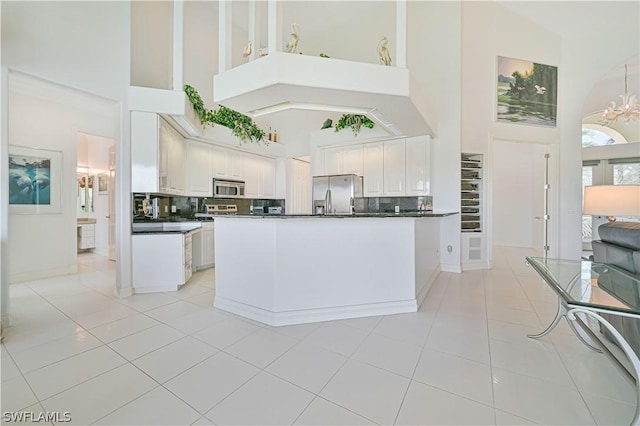 kitchen with light tile patterned floors, stainless steel appliances, white cabinets, dark countertops, and an inviting chandelier