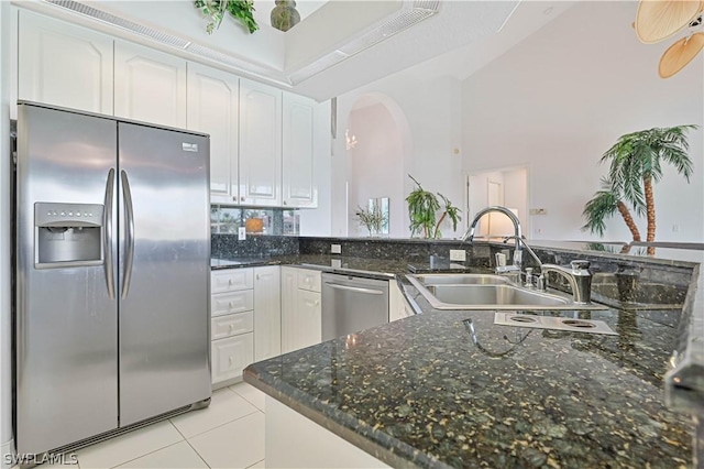 kitchen featuring arched walkways, light tile patterned floors, stainless steel appliances, white cabinetry, and a sink