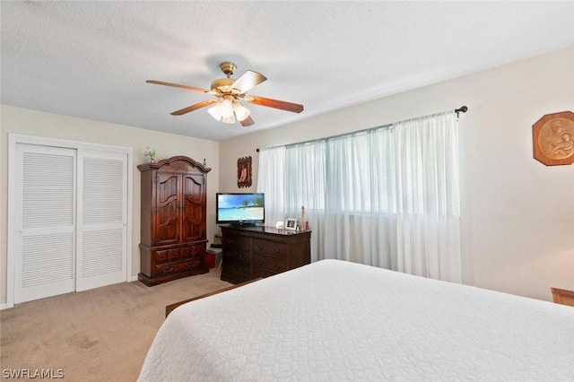 bedroom featuring a textured ceiling, ceiling fan, light carpet, and a closet