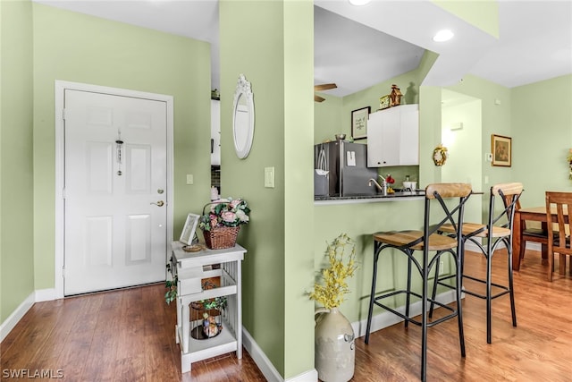 kitchen featuring ceiling fan, hardwood / wood-style flooring, white cabinets, a breakfast bar area, and stainless steel refrigerator