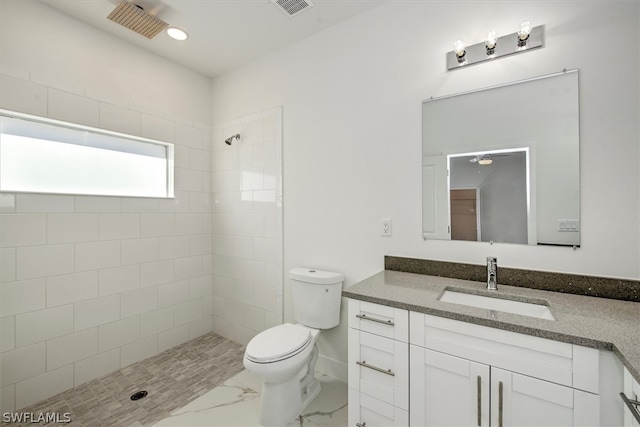 bathroom featuring a tile shower, vanity, and toilet