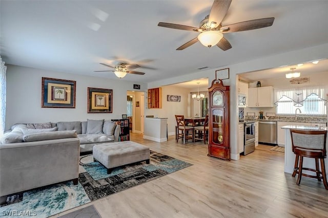 living room featuring ceiling fan with notable chandelier, light hardwood / wood-style flooring, and sink