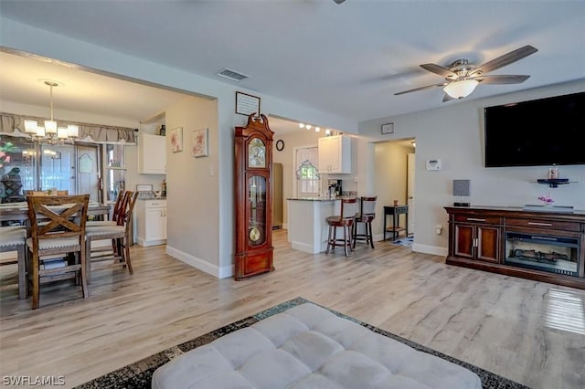 living room featuring a wealth of natural light, light hardwood / wood-style floors, and ceiling fan with notable chandelier