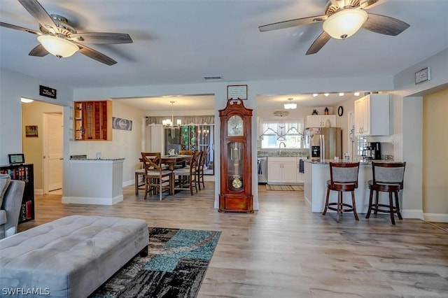 living room with ceiling fan with notable chandelier and light wood-type flooring