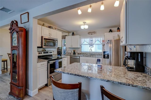 kitchen featuring sink, hanging light fixtures, appliances with stainless steel finishes, white cabinets, and light wood-type flooring