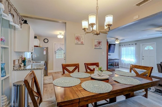 dining area with sink, ceiling fan with notable chandelier, and light wood-type flooring