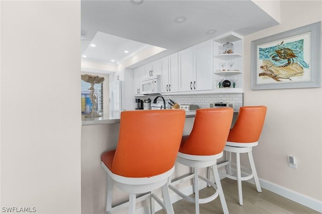 kitchen featuring white cabinetry, light hardwood / wood-style flooring, backsplash, crown molding, and a tray ceiling