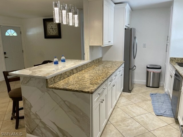 kitchen featuring white cabinetry, a kitchen breakfast bar, light stone countertops, hanging light fixtures, and stainless steel refrigerator