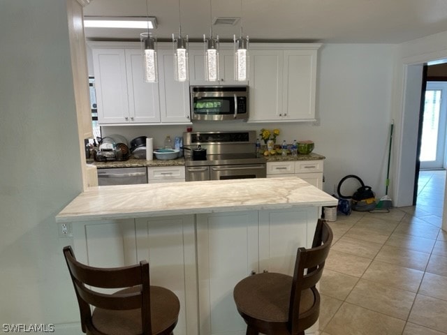 kitchen featuring white cabinetry, stainless steel appliances, decorative light fixtures, a breakfast bar, and light tile floors