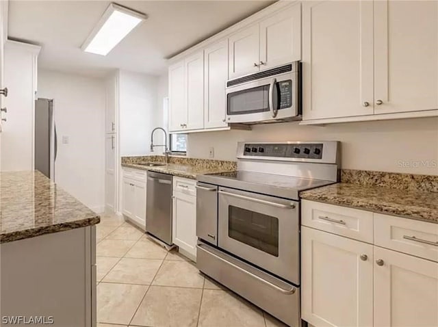 kitchen featuring stone countertops, white cabinets, sink, light tile floors, and appliances with stainless steel finishes