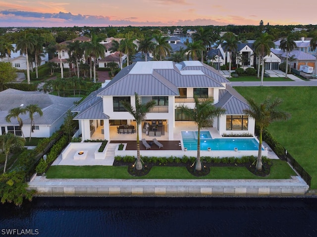 back house at dusk featuring a swimming pool with hot tub, a yard, a patio, a water view, and a balcony