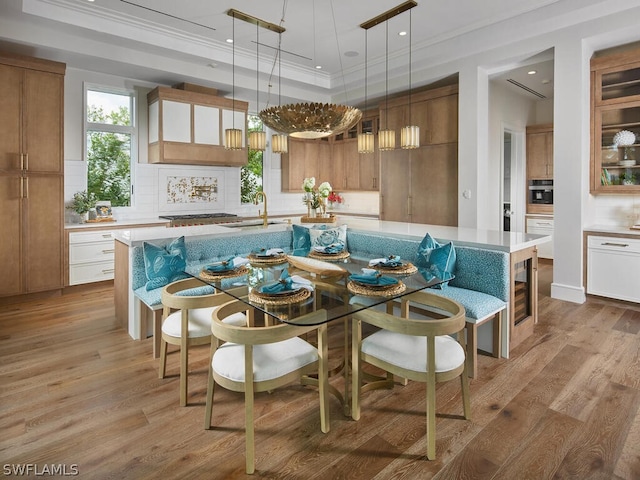 dining space with crown molding, sink, a tray ceiling, and light hardwood / wood-style flooring