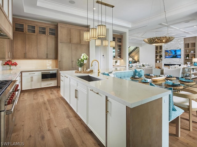 kitchen featuring sink, hanging light fixtures, an island with sink, white cabinets, and range with two ovens