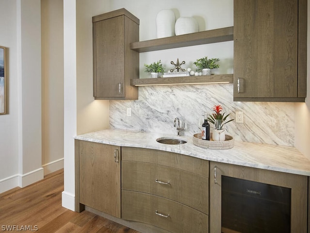 bar with tasteful backsplash, dark hardwood / wood-style flooring, light stone countertops, and sink