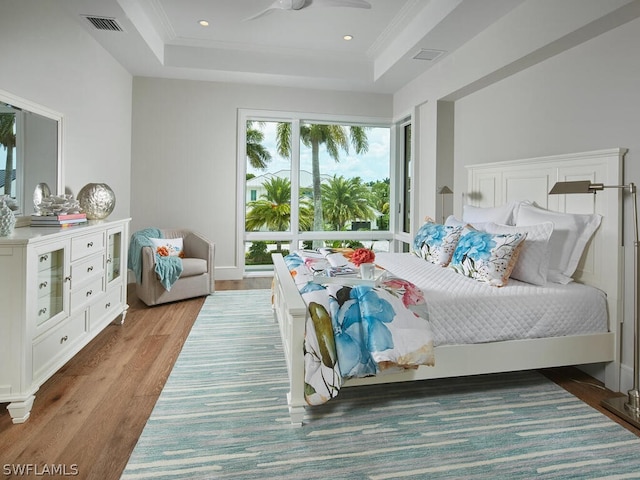 bedroom with wood-type flooring, crown molding, ceiling fan, and a tray ceiling